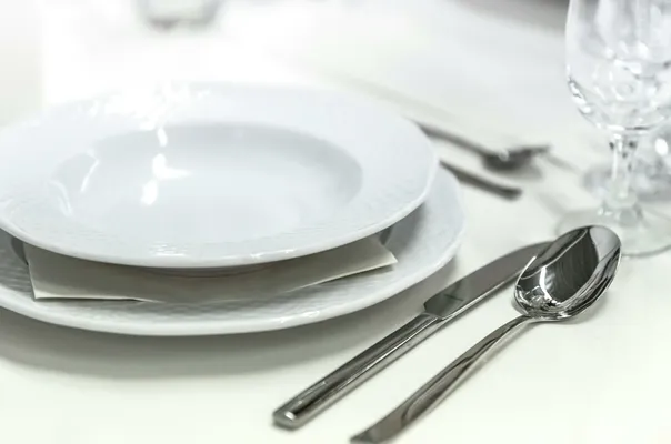 Elegant dining table with white porcelain plates and silver cutlery elegantly arranged.