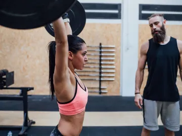 Young woman power lifting helped by her personal trainer