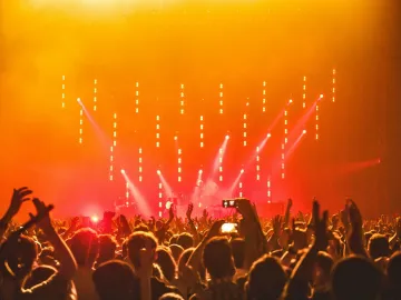Energetic crowd at a live concert with bright stage lights and hands raised in celebration.