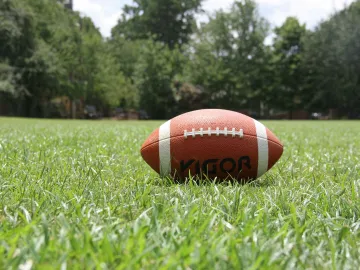 A close-up of an American football on a grassy field, highlighting outdoor sports in summer.