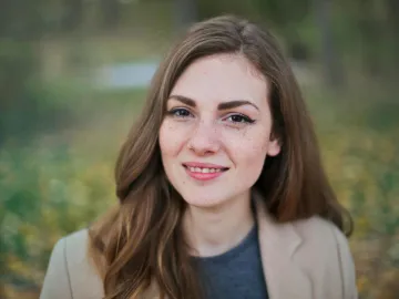 Close-up portrait of a smiling woman with freckles and long hair in a Budapest park during fall.