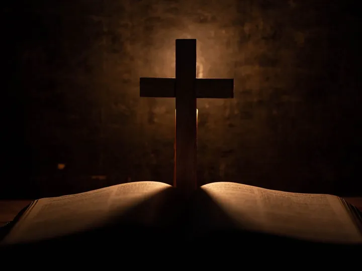 Cross with bible and candle on a old oak wooden table.