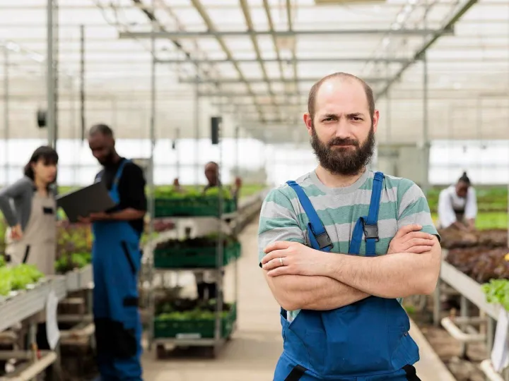 Portrait of confident man working in greenhouse while agricu