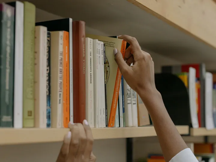 A person choosing a book from a library shelf showing diverse literature collection.