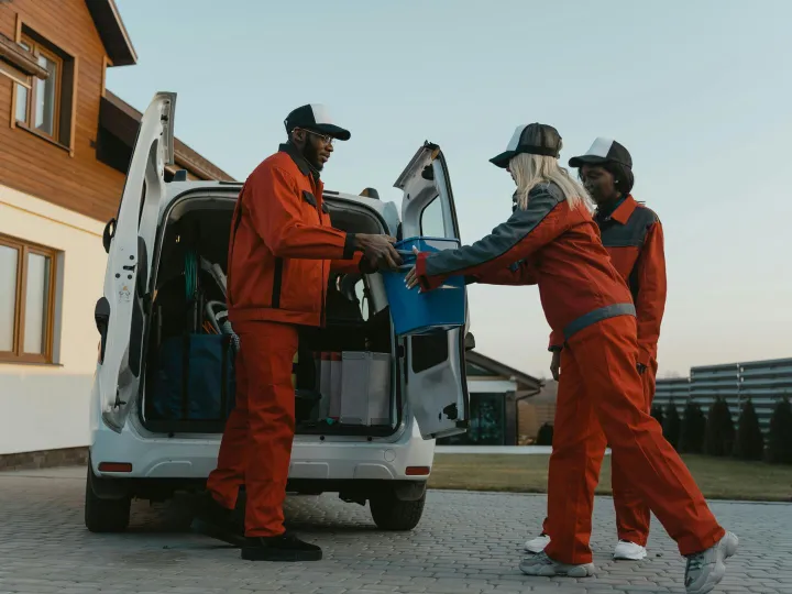Three adults in uniform unloading equipment from a
